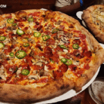 Large pepperoni, mushroom, and jalapeño pizza on a wooden table with text reading How Long Can Pizza Last in the Fridge – food storage and safety concept