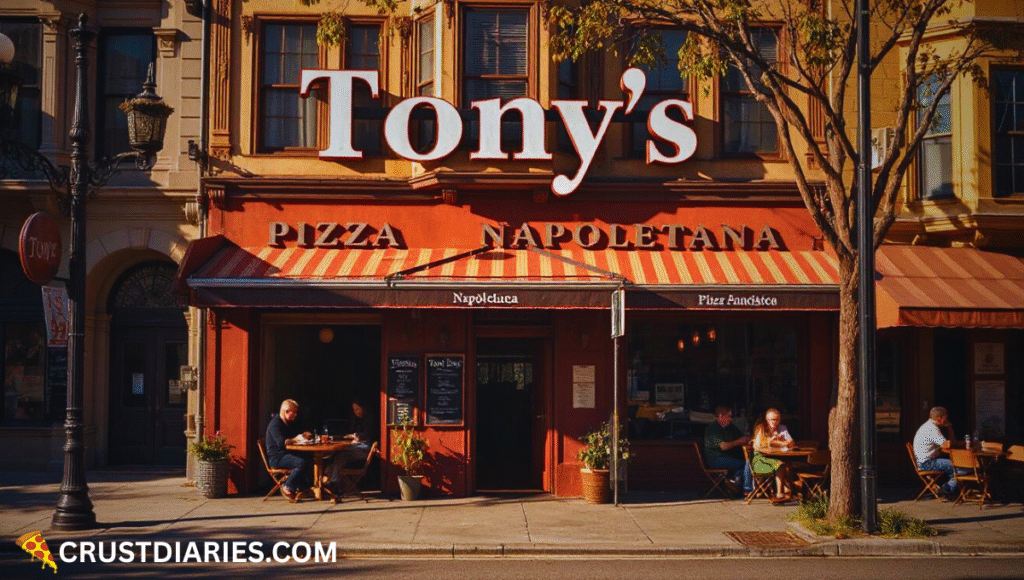 Street view of Tony’s Pizza Napoletana in San Francisco, CA, with its name clearly displayed on the sign above the entrance, colorful building facades, and customers dining at outdoor tables in warm afternoon sunlight.